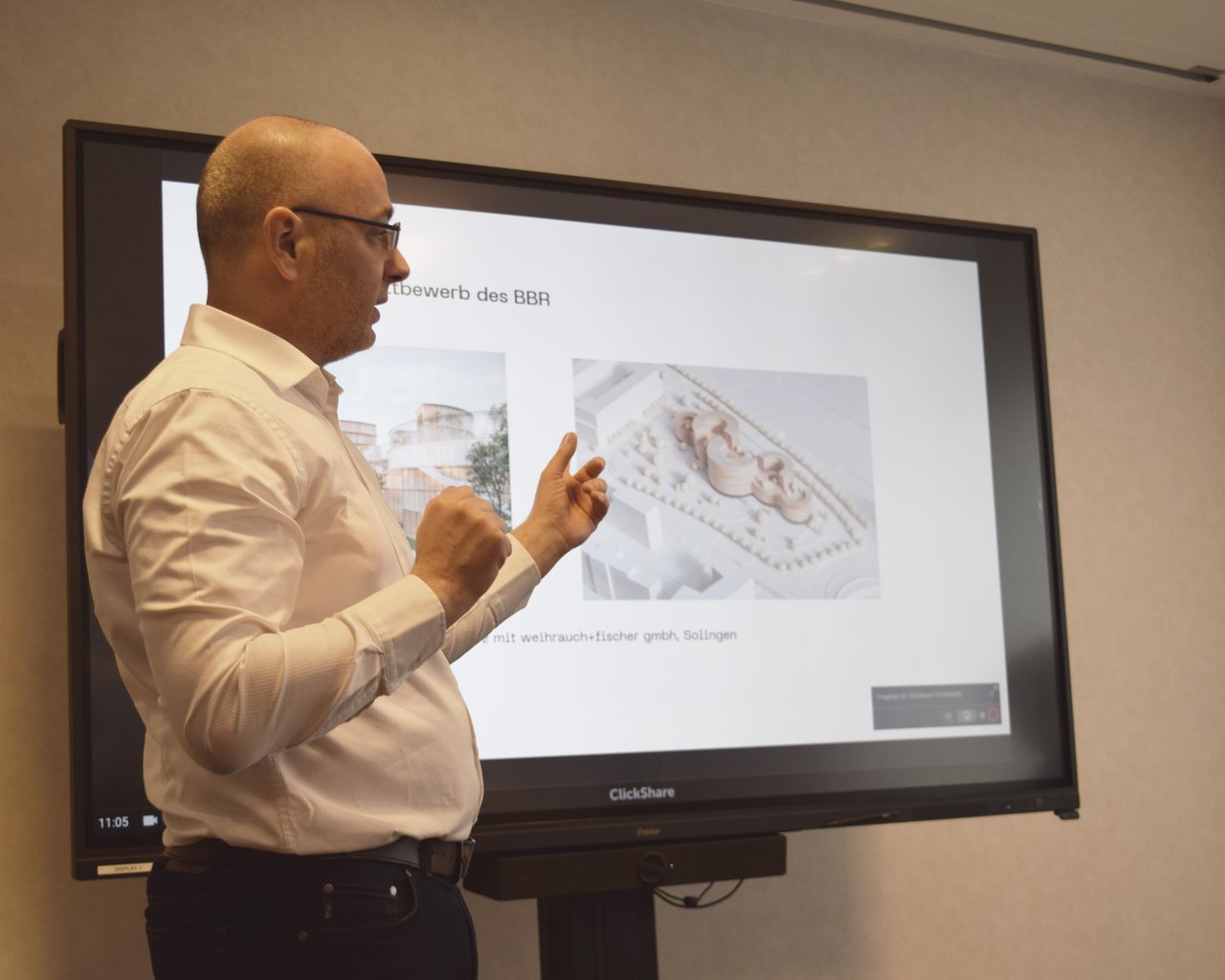 Toni-Christian Mohs hält eine Präsentation über den Bau. Hinter ihm eine Powerpoint Folie mit dem Entwurf der Architekten