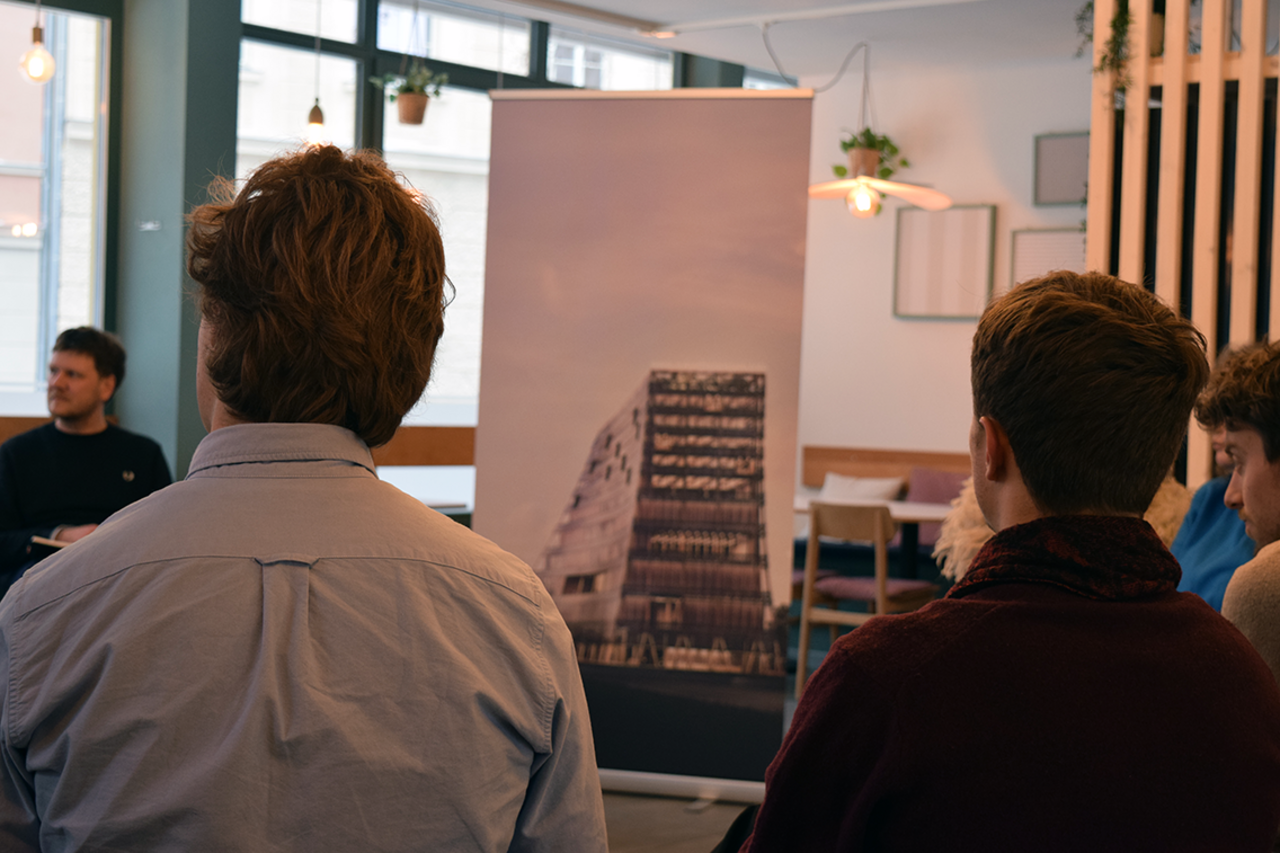 Rücken zweier Studenten. Dazwischen, im Hintergrund, sieht man das Banner des Zukunfgtszentrums mit der Visualisierung des geplanten Hochhauses