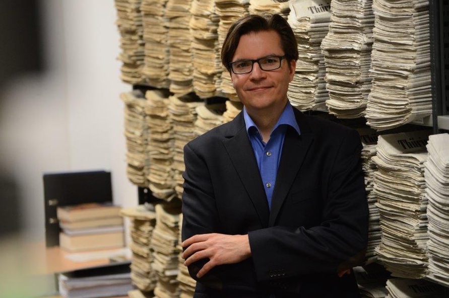 Jan Schönfelder vor einer Wand Zeitungen